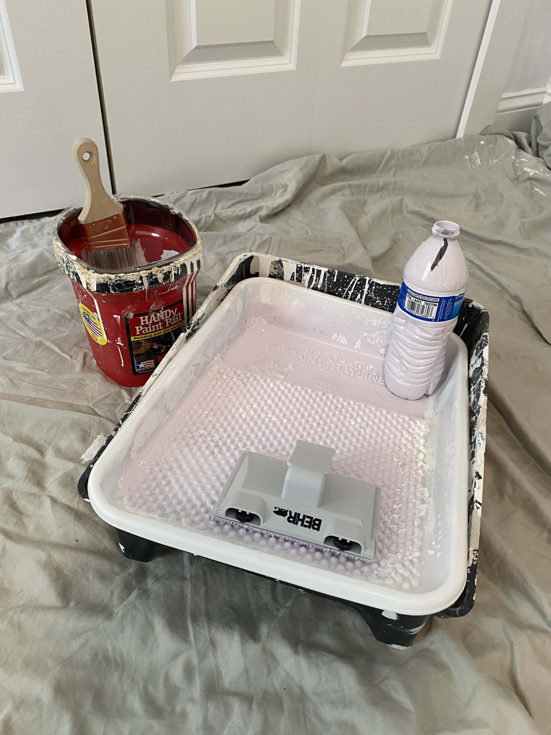 Painting roller tray with edger, water bottle and painter's pail next to it.